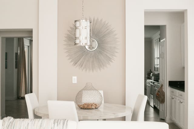 Breakfast nook with a round table and white chairs, with open doorways showing the hallway on the left and the kitchen on the right.